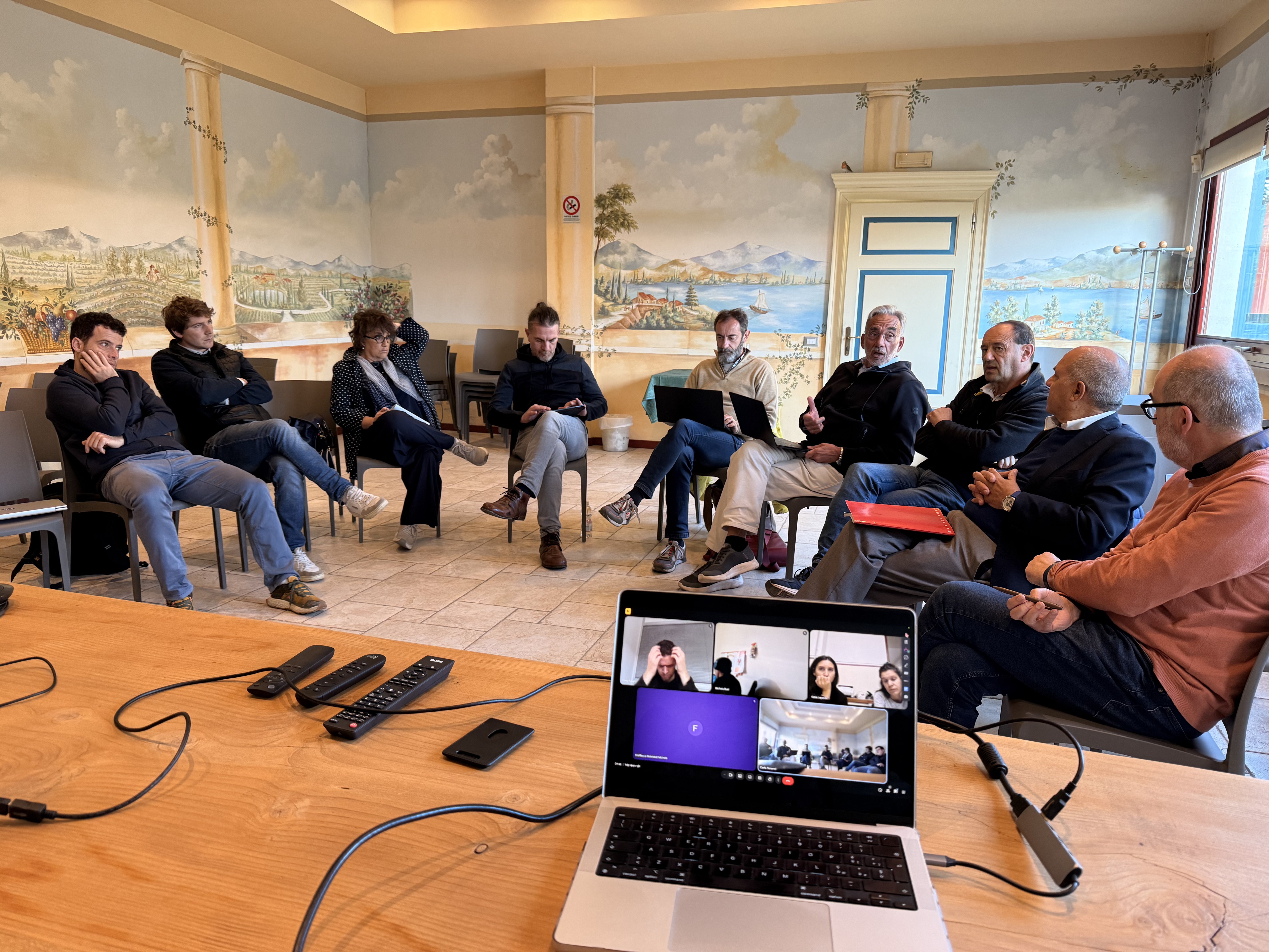 A group of colleagues in a hybrid meeting around a conference table with laptop video call
