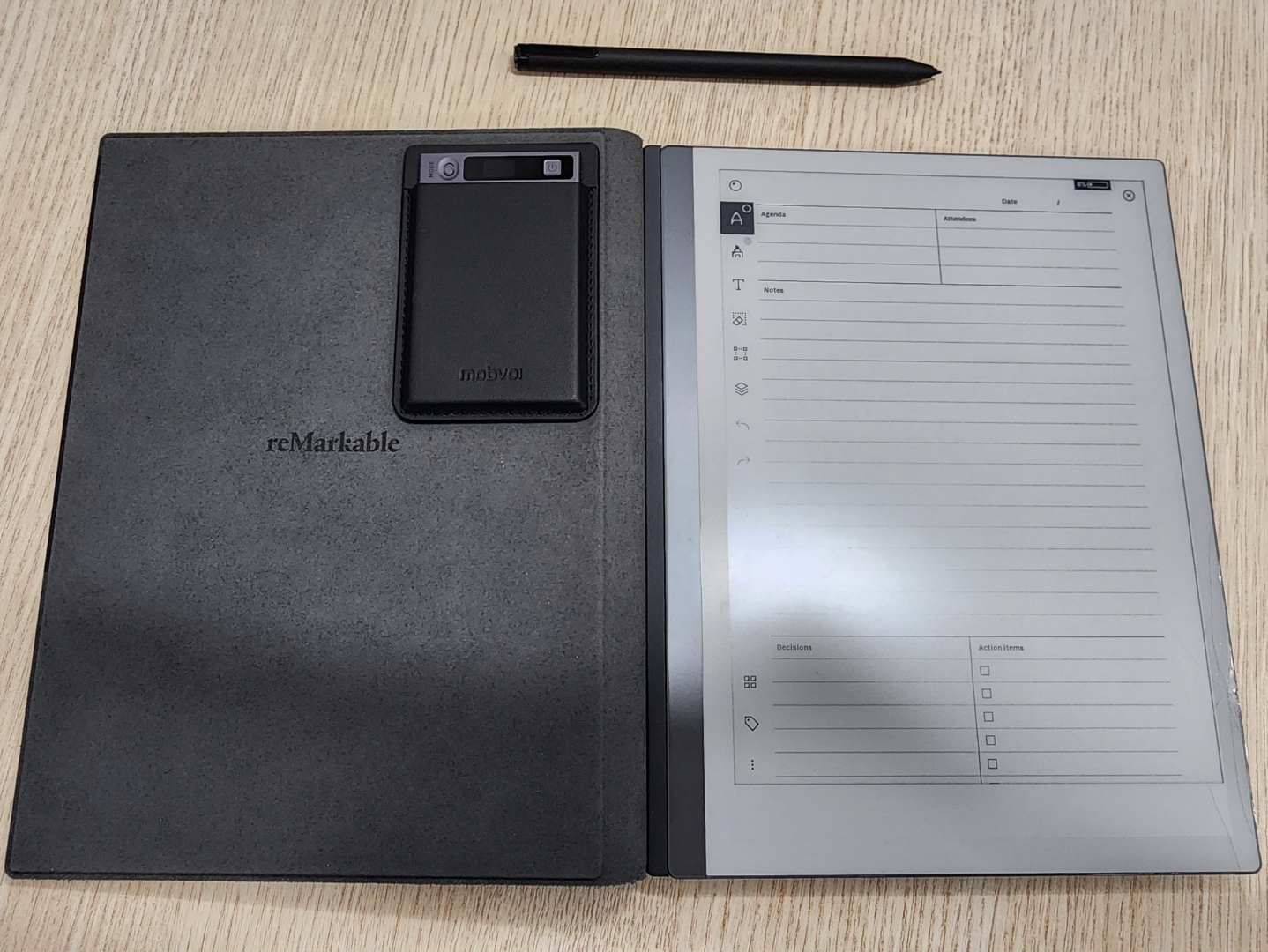 A reMarkable e-paper tablet open to a meeting notes template, with stylus, on a wood desk
